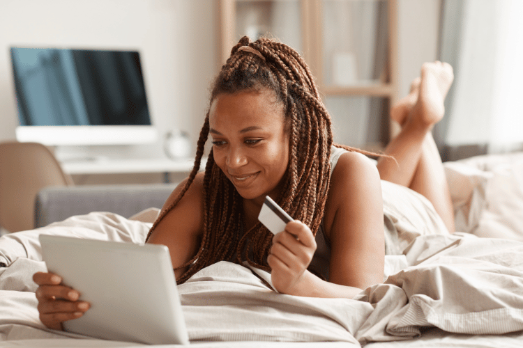 A young woman lying on a bed and holding credit card for online shopping